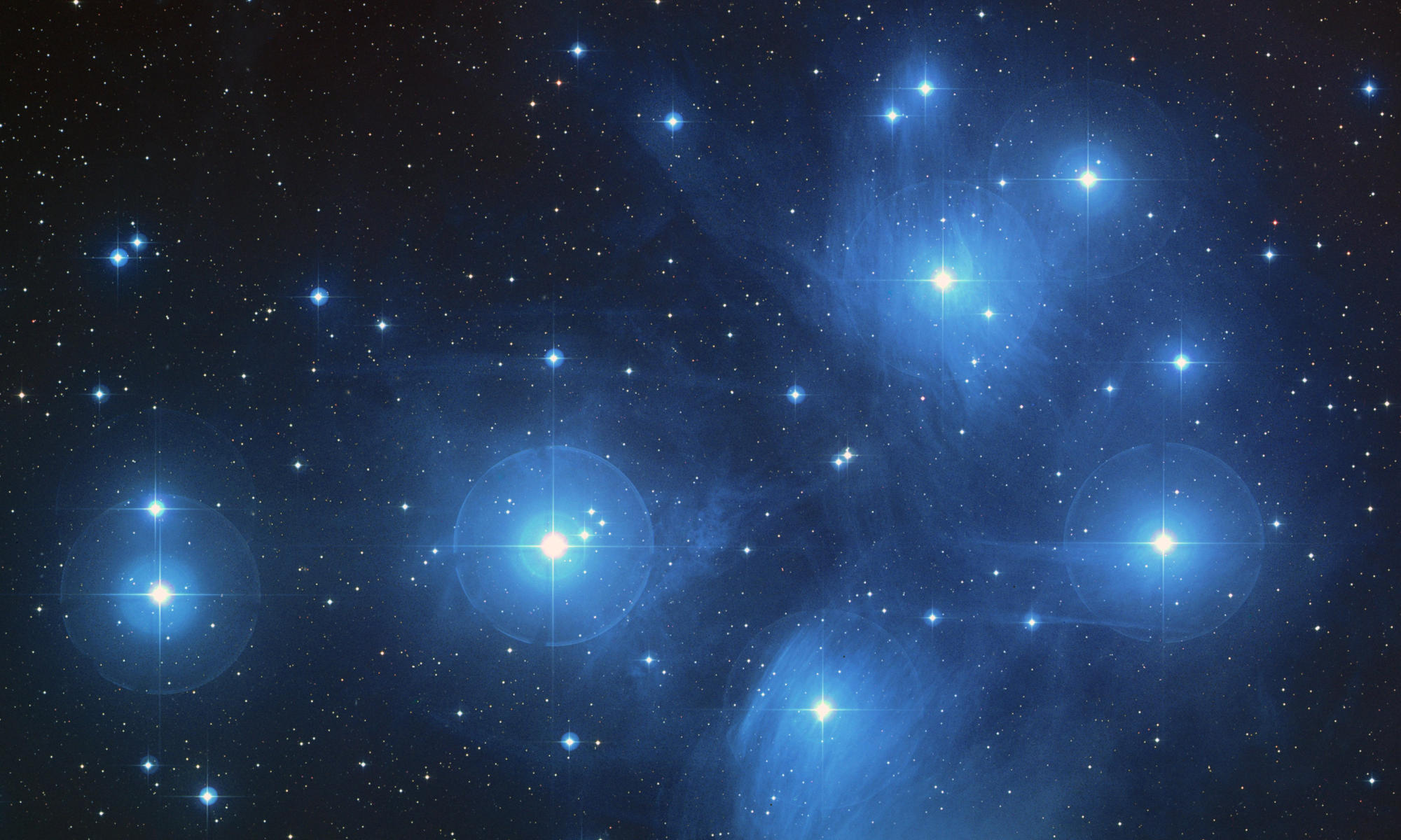Primo piano astronomico di brillanti stelle azzurre con effetti di alone e tenue nebulosità blu su sfondo nero