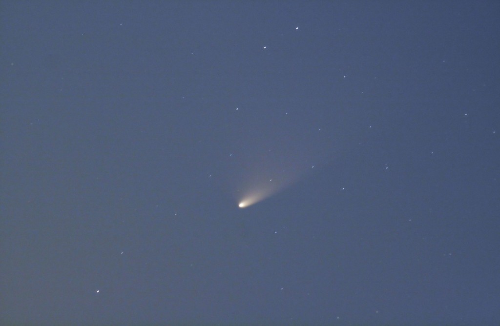 Cielo blu scuro con una cometa dalla testa luminosa e coda tenue tra stelle sparse