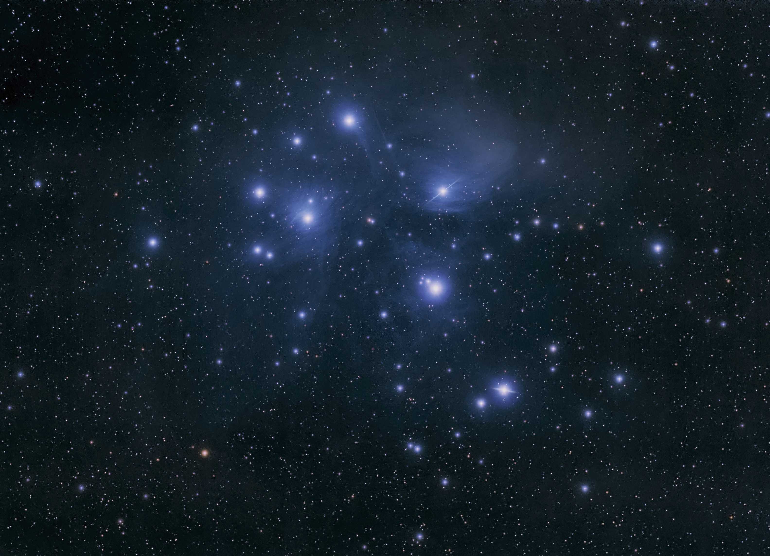 Ammasso stellare con brillanti stelle azzurre avvolte da una tenue nebulosa a riflessione su uno sfondo scuro punteggiato di stelle