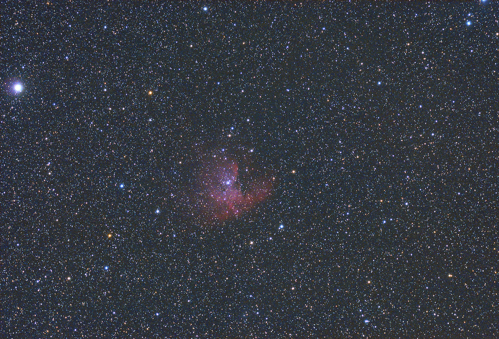 Campo stellare con una piccola nebulosa rosa brillante tra stelle sparse su fondo scuro